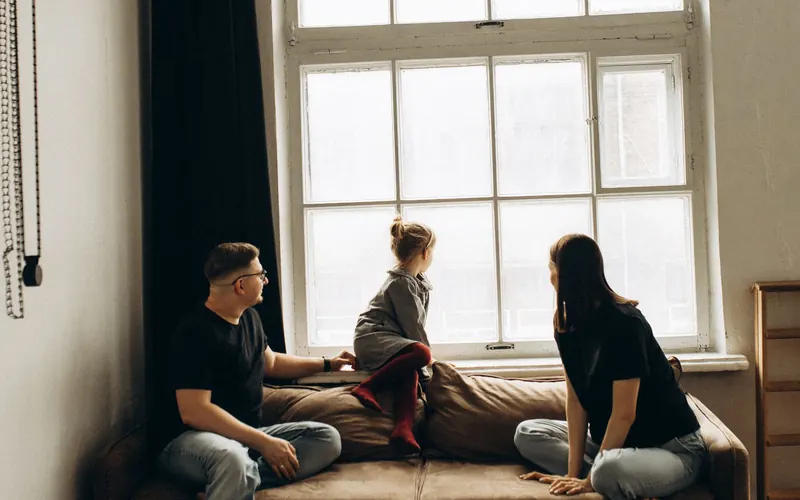 Famille assise sur un canapé près d'une grande fenêtre dans un salon chaleureux