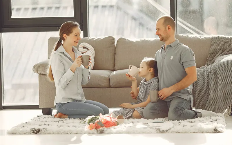 Parents et enfant jouant sur le tapis d'un salon lumineux et chaleureux