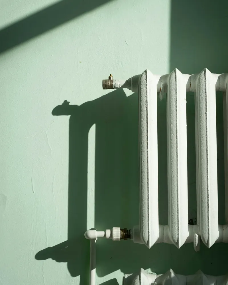 Radiateur en fonte blanc sous la lumière du soleil contre un mur vert pâle