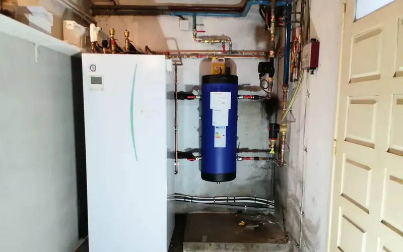 Module intérieur de PAC air-eau au sol et ballon d'eau chaude installés dans un garage.